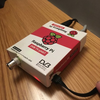 A raspberry pi shoved into the cardboard box for the Raspberry Pi TV HAT.