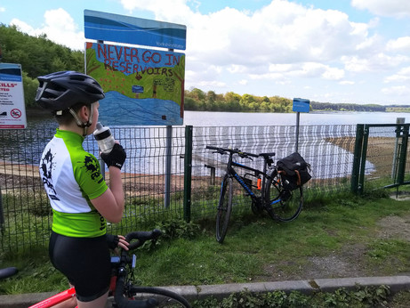 Boy in cycling kit drinking from a water bottle in front of reservoir sign