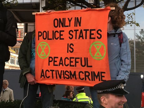 A banner reading “only in police states is peaceful activism crime”