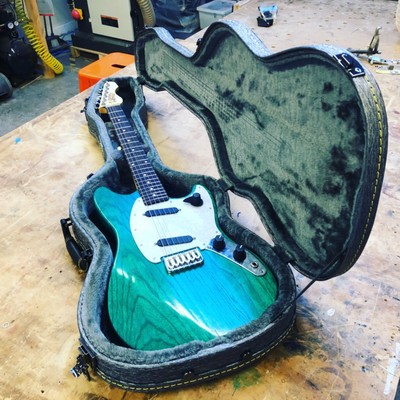 A green offset electric guitar sat in a case that I hand made