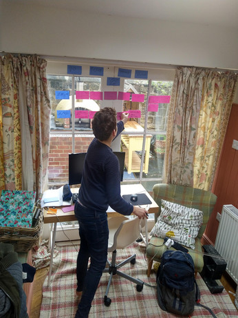 Boy sticking sticky notes on window behind a desk with curved monitor, laptop and swivel chair