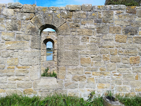 Old ruined building with arched window, through which is another similar window looking out over an estuary