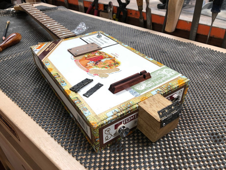 My guitar box guitar on the workbench with the new bridge in place and the broken old one on top.