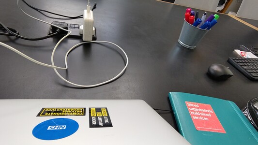 Black linoleum desktop with laptop, notebook, wires and pens