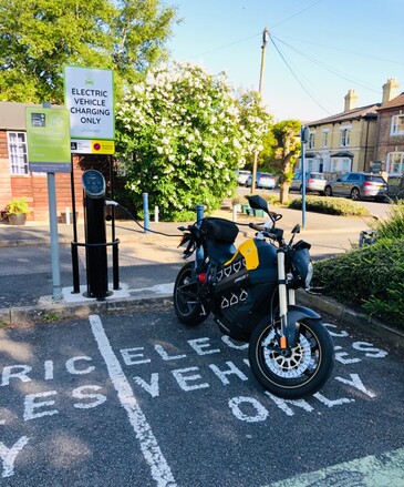 An electric motorbike parked at a charge point in a sunny car park