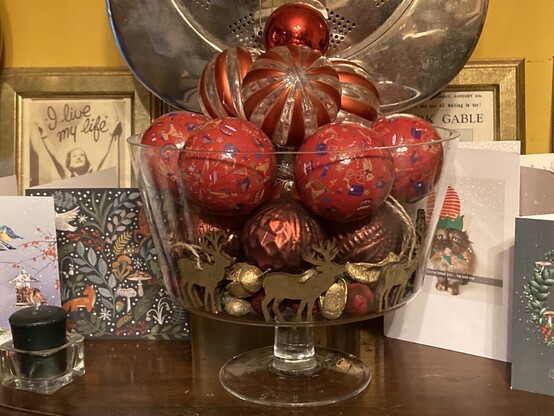 A large trifle bowl filled with red palette Christmas baubles, a few wooden reindeer and some bits of gold potpourri.