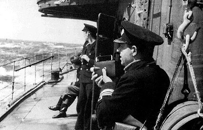 Plawski in uniform on the deck of his ship, holding a camera