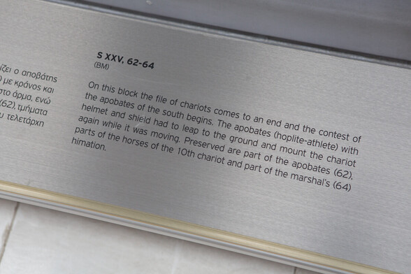 Plaque of museum exhibit, explaining that it depicts the end of a line of chariots, with the apobates (hoplite athletes) in helmet and shield required to jump off their chariots and then jump back on while they were still in motion