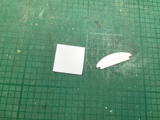 On the grubby green cutting mat the square-shaped compartment divider, and the flattened mushroom-shaped roof strengthener are seen after being snapped from the main sheet.