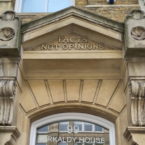 Ornate classical stonework above a window. In stone relief the words FACTS NOT OPINIONS. On the glass in modern lettering the number 99 and words KIRKALDY HOUSE 