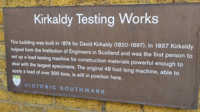 Sign on yellow London brick wall: "Kirkaldy Testing Works
This building was built in 1874 for David Kirkaldy (1820-1897). In 1857 Kirkaldy helped form the Institution of Engineers in Scotland and was the first person to set up a load testing machine for construction materials powerful enough to deal with the largest specimens. The original 48 foot long machine, able to apply a load of over 300 tons, is still in position here.
Historic Southwark"