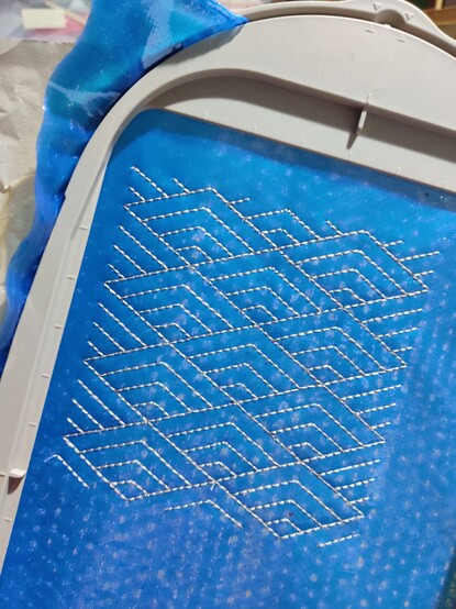 Large machine stitches in a diamond pattern on a variegated blue plastic background in a large machine embroidery hoop