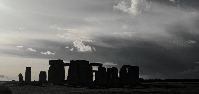 Black and white image of Stonehenge in the early evening, a dramatic cloud behind it