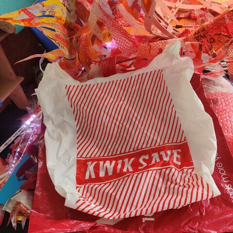 A KwikSave bag with a red design on white.
The background is red and orange heat pressed LDPE sheets and flames, and LEDs attached to white PVC strips (waiting to be covered with plastic flames)