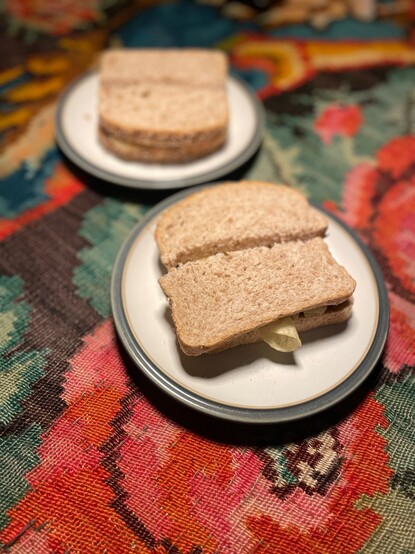 Two rounds of crisps sandwiches on plates on a colourful rug, one in focus, one out.