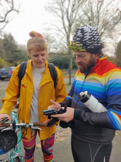 India,  holding a bike, talking to Stewart, who is taking details on a mobile phone.

They are standing in a car park, with a park in the background