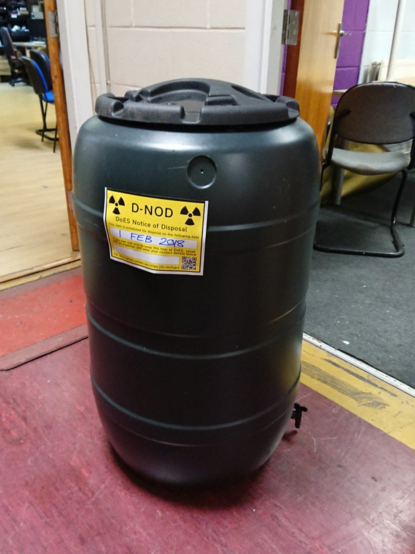A water butt with a yellow rectangular sticker on it saying: "DoES Notice of Disposal.  This item is scheduled for disposal on the following date" and underneath is a box where the user can write in a date.
