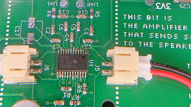A green circuit board with an assortment of components soldered to it, including a chip with lots of closely-spaced pins.