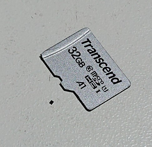 A micro-SD card on a white table with a tiny black dot next to it 