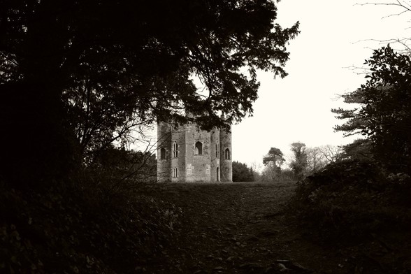 A sepia-toned black-and-white image of Blaise Castle, seen from a distance and framed by trees. It's not a proper castle, it's a folly.