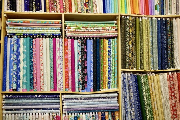 Loads of fabrics lined up on shelfs, all sorts of colours and patterns