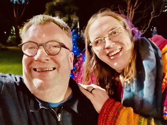 Photo of Jae and James smiling in front of Christmas lights