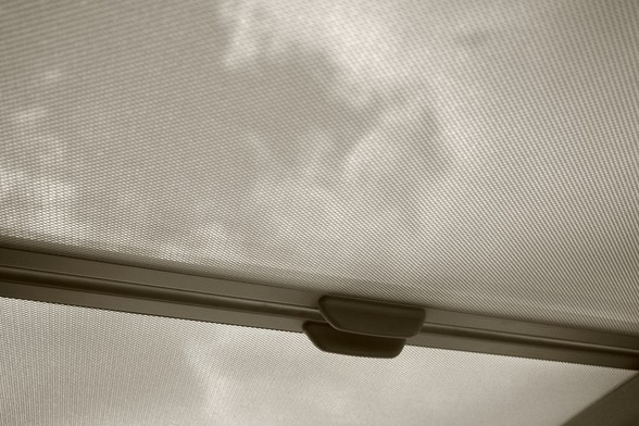 Looking up through the glass ceiling of a car, partially obscured by the sun blind