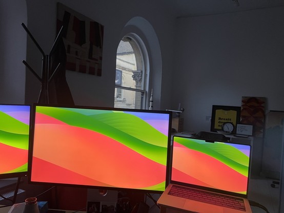 a colourful screensaver romps across three computer screens in an otherwise dimly lit, gloomy room