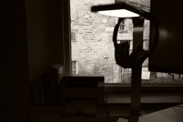 a view through a window, partially obscured by a lamp, some headphones, and office paraphenalia