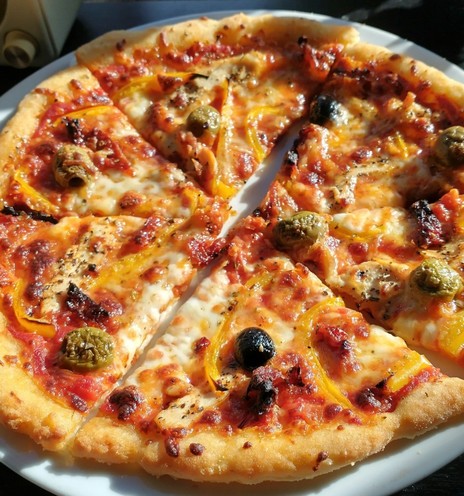 A close up of a thin 11'' gluten free pizza. The toppings include olives and yellow bell peppers.