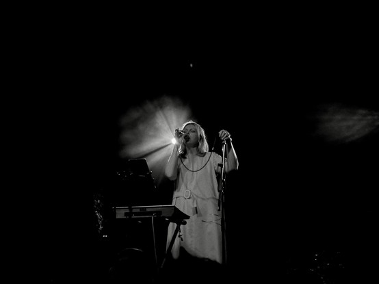 Moody black and white photo of Jane on stage, singing into a mic   A spotlight shines from just behind her head 
