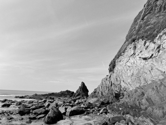 Beach view in black and white with pointy rock shaped like a witch’s hat