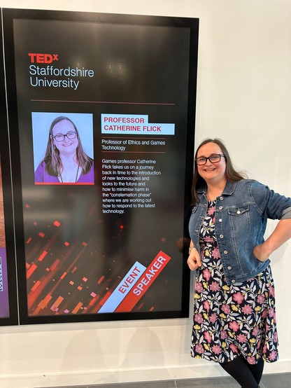 A picture of me standing next to a sign with my name and profile on it as a speaker at TEDxStaffordshireUniversity 