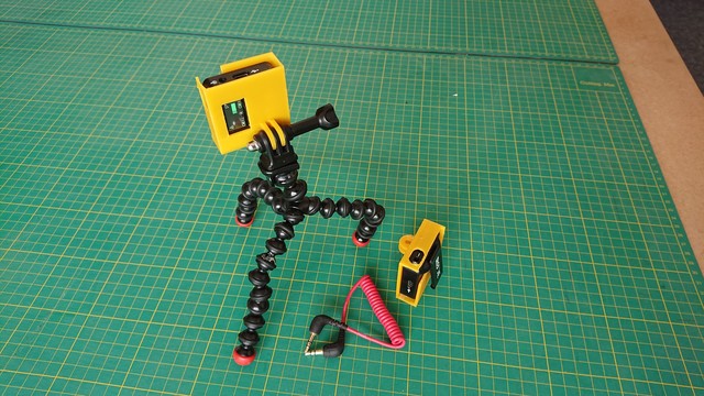 A small rectangular yellow box sits on top of a Gorillapod tripod, next to another one on a table but turned round. There's a hole in the top of them so a rectangular mic module can slide in, and a slot to allow the clip from the module to hold it in place.

At the base of the yellow boxes are the two protruding slots to mount on a GoPro mount; and there are cutouts allowing access to the power button, etc. 
