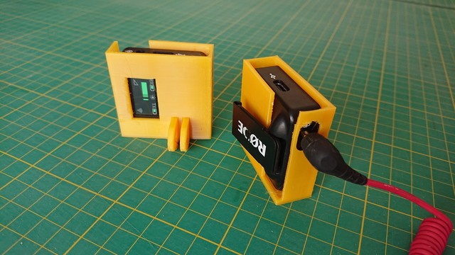 A closer shot of the modules in the last photo, both sat on a table.

Through a cutout on the receiver module sleeve you can see the receiver screen showing the audio level, and the mic module has a 3.5mm jack plugged in through a hole in the sleeve 