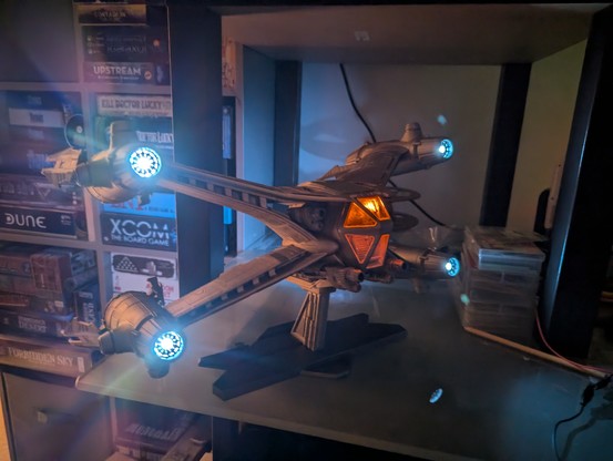 3d printed spaceship (with lights) assembled on a stand - a Starfury small 1 person fightercraft from Babylon 5. This time in the dark so you can see the lights much better. Orange cockpit & bright white engine glows