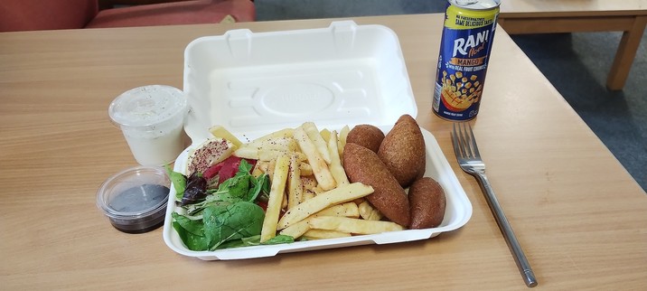 Kibbehs with chips and salad in a white takeaway box with a mango juice and a fork beside the box.