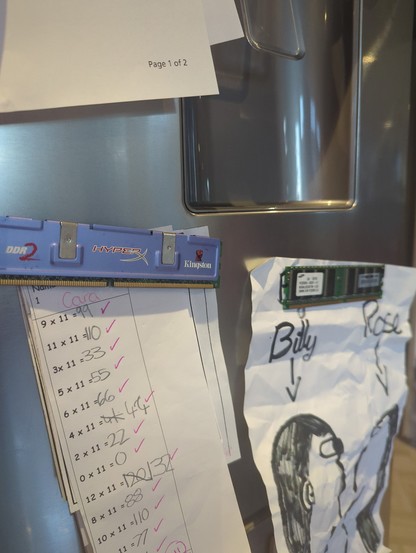 a ddr2 Kingston RAM module used as a fridge magnet to hold paper. A child's times table test sheet and childs drawing are secured this way