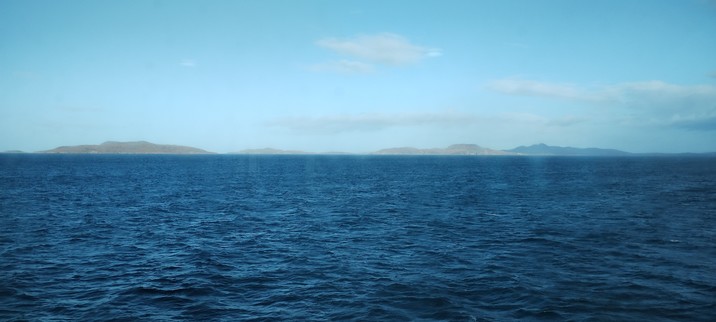 A view of the sea, quite dark shades of blue, and sky with a couple of islands on the horizon