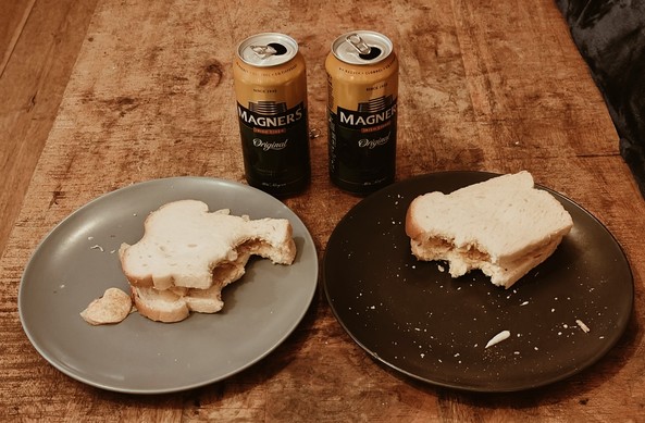 Two plates, each with a crisp sandwich on it, and two cans of Magners coffee. A bite or two has been taken out of each sandwich. 
