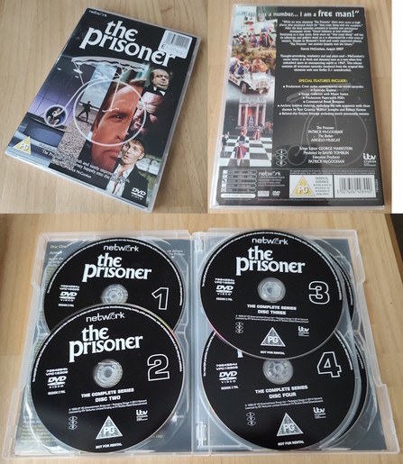 A high-angle, full studio shot shows “The Prisoner: The Complete Series” DVD box set in its entirety, open atop a wooden surface. The shot is well-lit and focuses on the visual details of the box set and its contents.

At the top-left, a shrink-wrapped DVD case lies flat, displaying the cover art of “The Prisoner.” The artwork includes dramatic imagery and a title overlay. To its right and slightly behind, the back of the DVD case is visible, featuring a summary of the series, special features, and production details. Behind the two DVD cases, are the four black DVDs in their clear plastic cases. The disks are labelled “1,” “2,” “3,” and “4” in distinct, white numerals. Each disc includes the “network,” “The Prisoner,” “DVD Video,” “The Complete Series,” ITV logo, and PG rating.

The DVDs appear to be arranged in an organized manner, showcasing the full set as a collectible item. The wooden surface and lighting highlight the visual details and text on the DVDs and cases.
