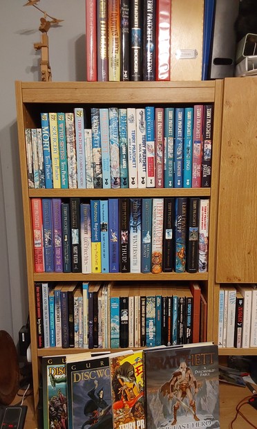 A bookshelf full of Terry Pratchett books, mostly in hardback, and also the GURPS Discworld RPG books.