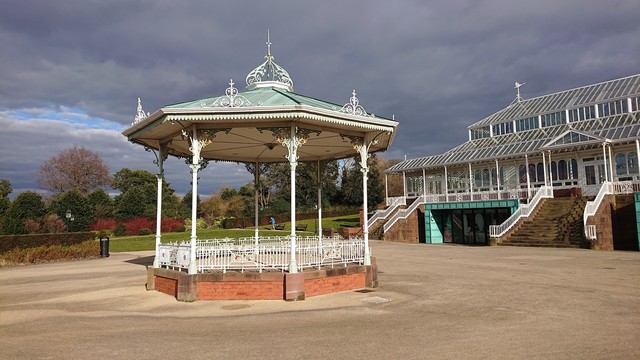 A pretty octagonal wrought iron bandstand surrounded by a paved area in a park.  It's mostly painted white, with coloured highlights, and a green copper roof.  Just to one side of it is the Isla Gladstone conservatory, a relatively-recently restored Victorian glasshouse.

This is in Stanley Park in Liverpool, and while taking it I could hear the excitement of the crowd at one of Everton's last games at the nearby Goodison Park.