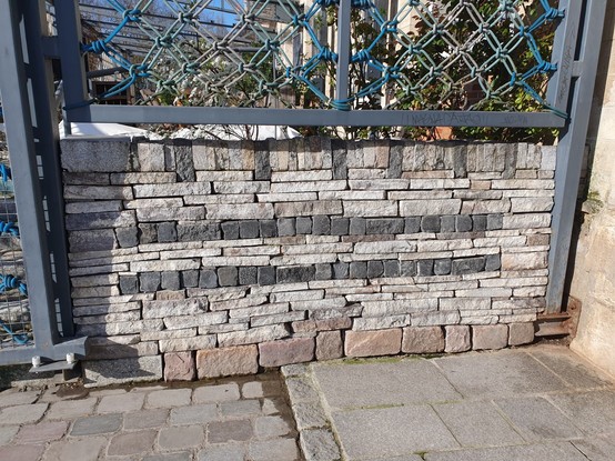 Short section of drywall, about waist high, made of light stone with two decorative dark stone courses.