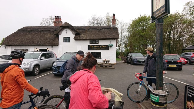 A group of cyclists stopped outside an old whitewashed brick pub with a thatched roof.  The sign on the side of it names it the Scotch Piper, and underneath proclaims "The oldest inn in Lancashire.  A.D. 1320"

Although strictly speaking, these days it's actually in Merseyside