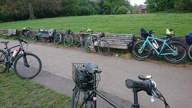 Lots of bikes of all types parked up on their stands or leaning against a low wall around the park benches spaced out along it, at the top of Camp Hill