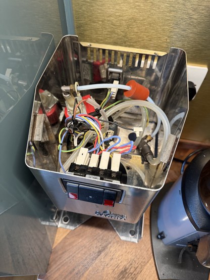 The top view of a partly dismantled coffee machine. Many coloured cables and tubes snake around. Parts are obviously missing.