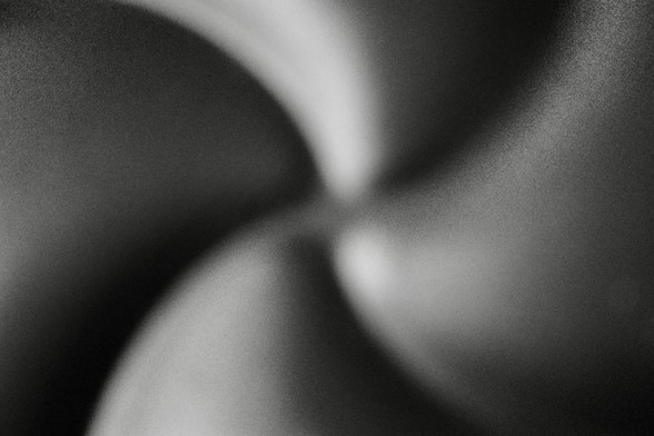 Abstract b/w photo - four blurred curving lines meet in the centre of the image. Like arms of a spiral galaxy. Actually it's the base of an air fryer pan. 