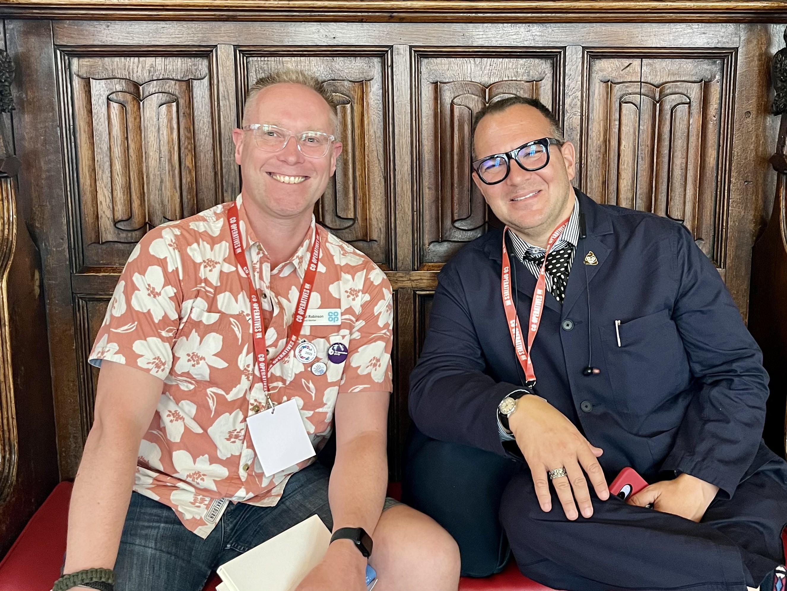 Image features two men (me in the left and Cory Doctorow on the right) looking into and smiling at the camera. They’re sat on a red cushion bench with their backs to an ornately carved oak panelled wall in Rochdale Town Hall’s Great Hall.