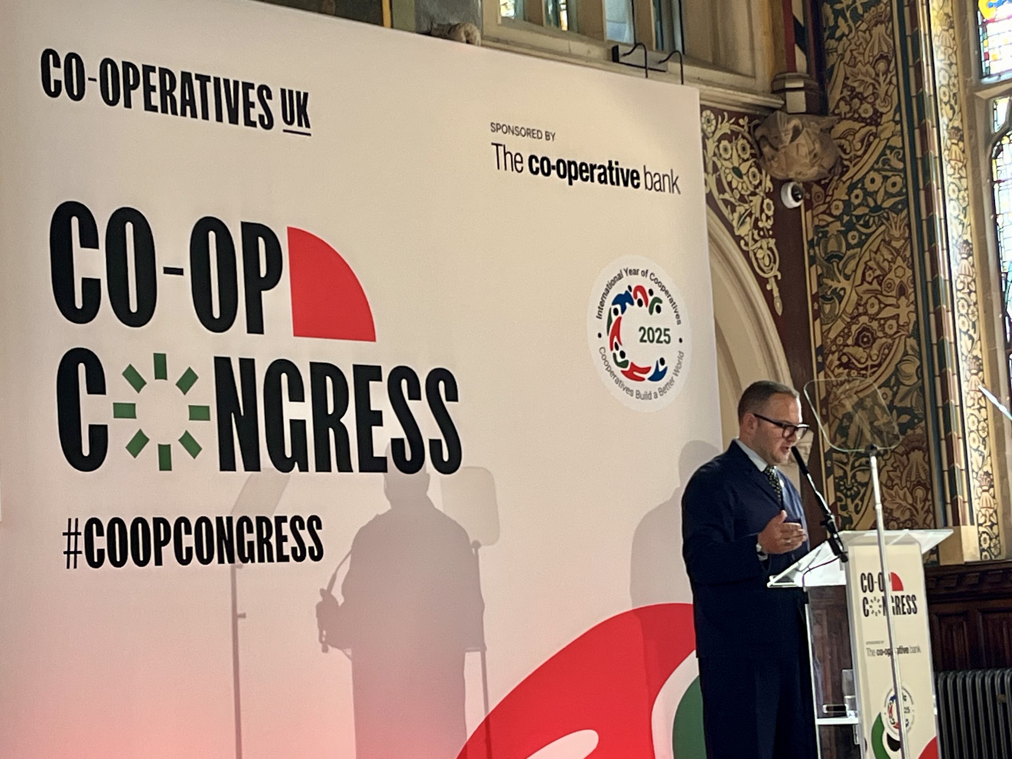 Image features Cory Doctorow on a raised platform in the Great Hall of Rochdale Town Hall with a backdrop from #CoopCongress